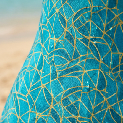 Close-up of a blue fabric with gold geometric patterns on a beach background