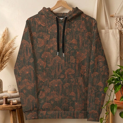 A pullover hoodie hanging on a wooden hanger against a warm beige wall, featuring an all-over botanical pattern in muted brown and rust tones over a dark charcoal base. The hoodie has black drawstrings with silver tips and a front kangaroo pocket.