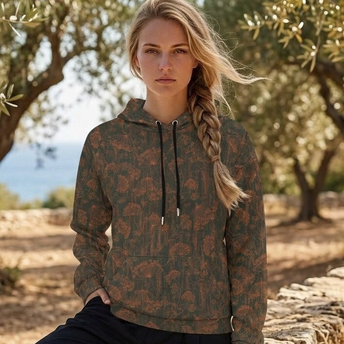 A woman wearing a dark olive green and brown patterned hoodie with black drawstrings, standing outdoors in a sunny, tree-filled environment.