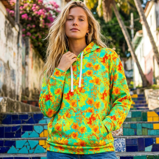 A woman wearing a bright green pullover hoodie with an orange and yellow floral pattern, standing on colorful mosaic outdoor steps.
